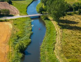 Luftaufnahme eines schmalen Flusses mit Brücke in Schleswig-Holstein – grüne Uferlandschaft und ein Kanufahrer in ruhiger Naturidylle.