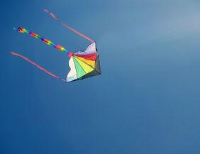 A colorful kite soars high in the clear blue sky. The long, colorful ribbons flutter in the wind.